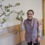 職員が室内で立っている様子。背後には植物が飾られている。