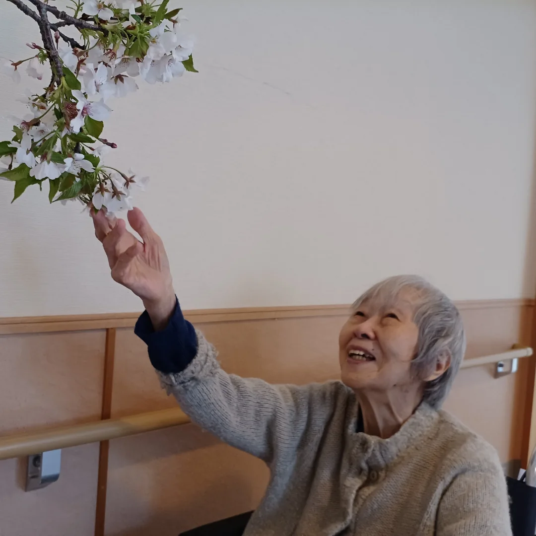 入居者が施設内の花を観賞し、笑顔で手を伸ばしている日常風景